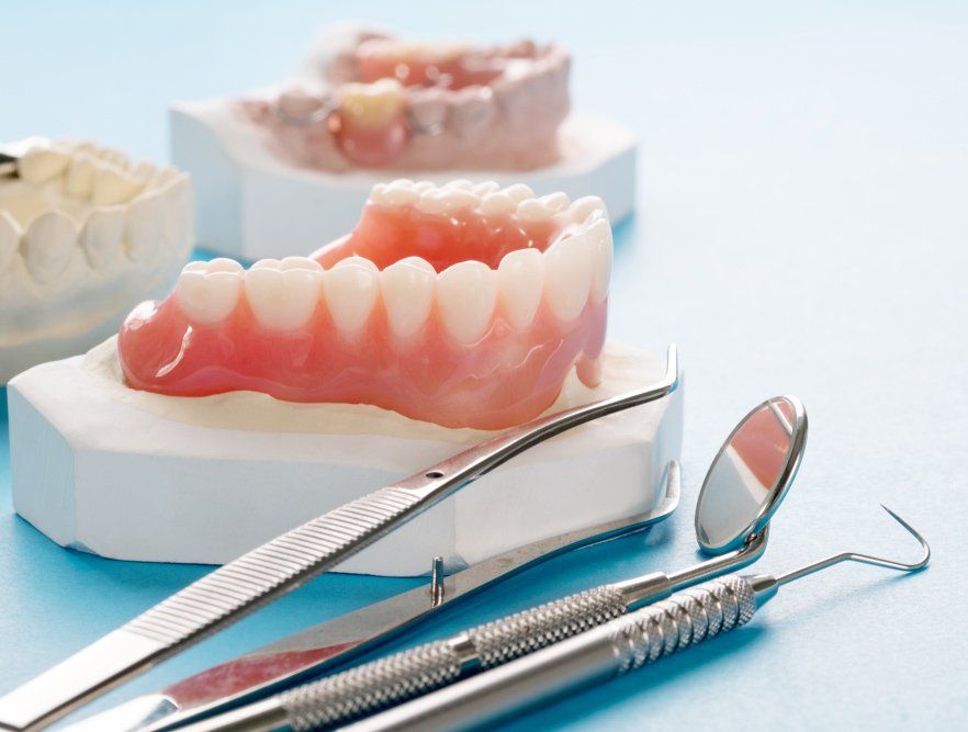 Close-up Complete Denture With Dental Tools On Blue Background — Maitland Dental Care In Maitland NSW
