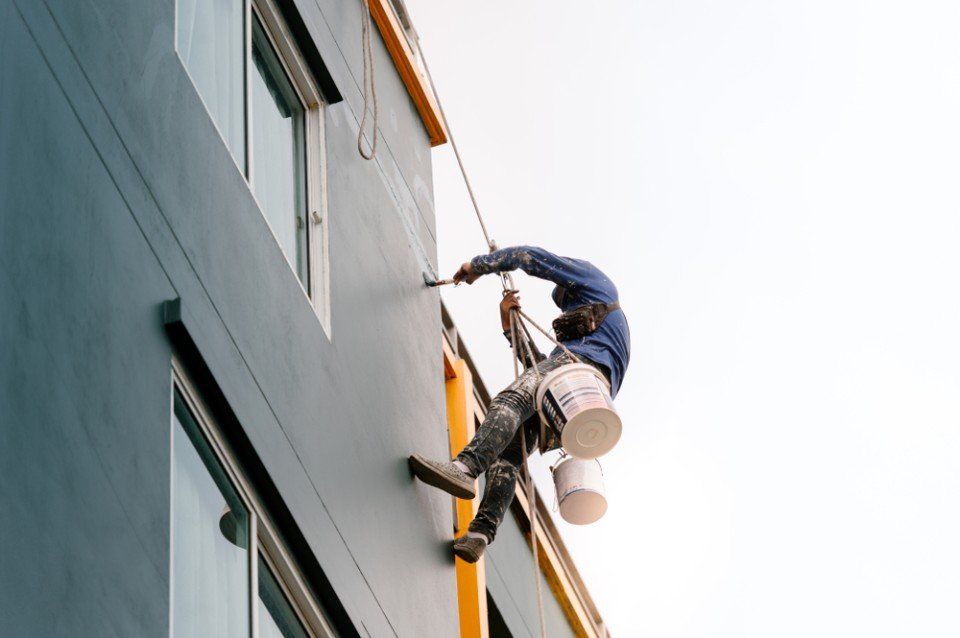 male workers painting building wall on the rope.