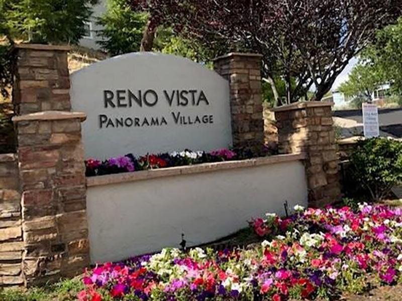 Entrance sign reading Reno Vista Panorama Village with stone pillars and colorful flowers.