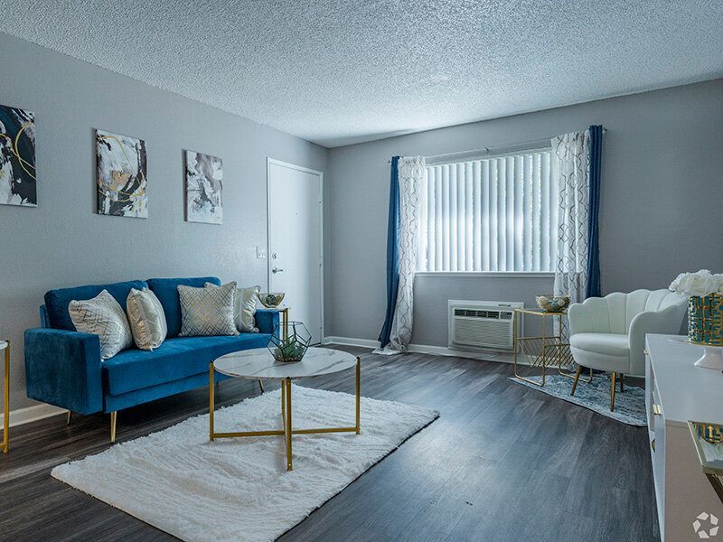 Living room in an apartment with a blue sofa, white chairs, and a marble coffee table near a window.