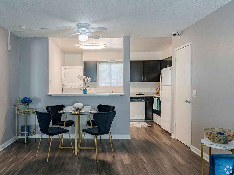 Open-concept apartment kitchen and dining area with round glass table and four blue chairs.
