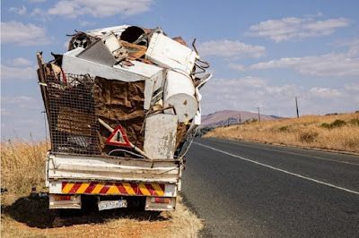 A truck filled with junk is parked on the side of the road.