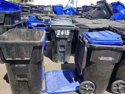 A pile of trash cans with blue lids are sitting on the ground.