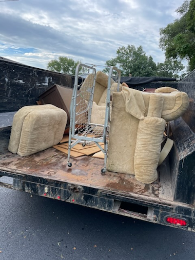 A dumpster filled with furniture is parked on the side of the road.