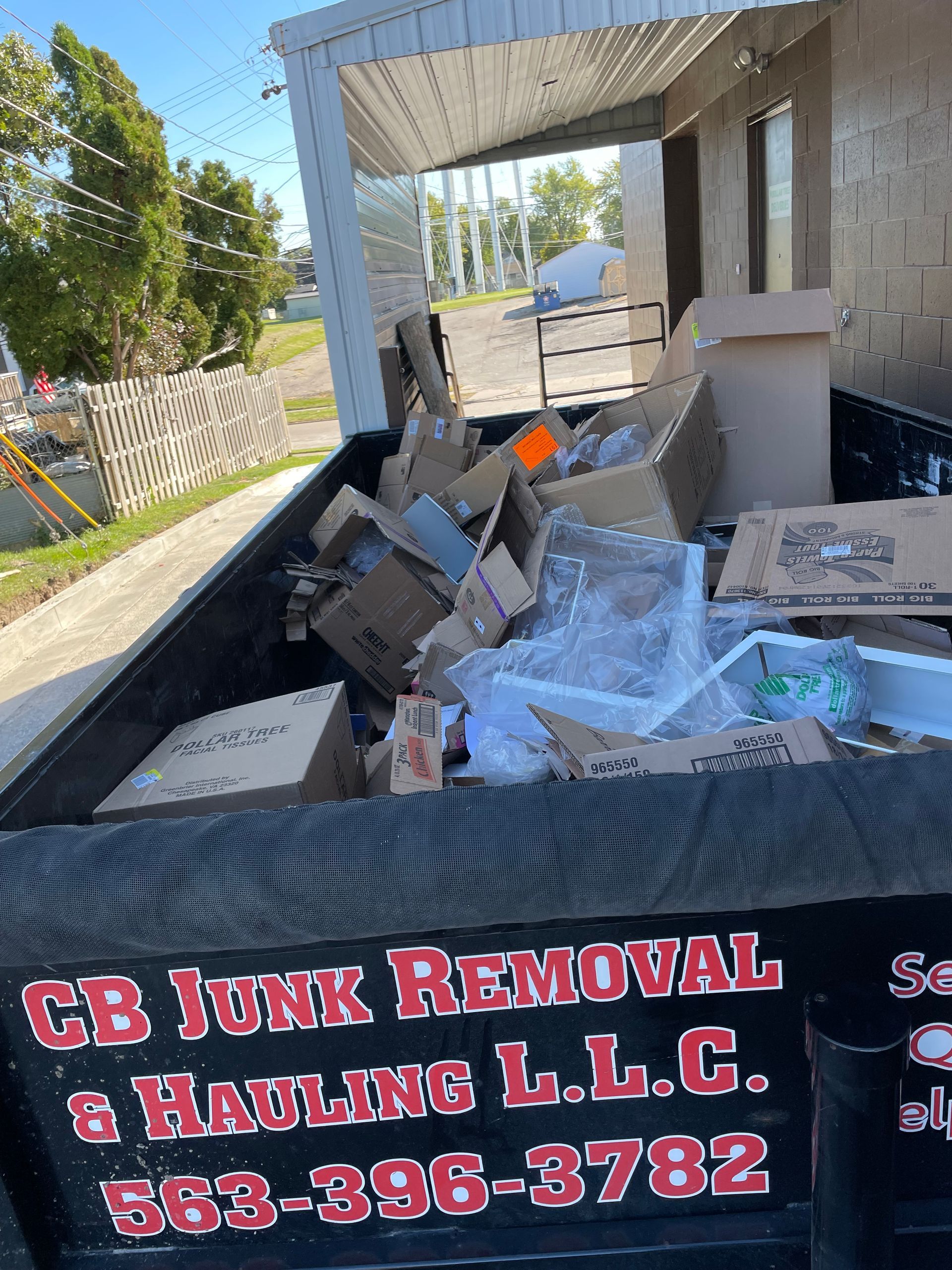Dumpster filled with cardboard boxes and debris, CB Junk Removal & Hauling L.L.C. truck, 563-396-3782 on the side.