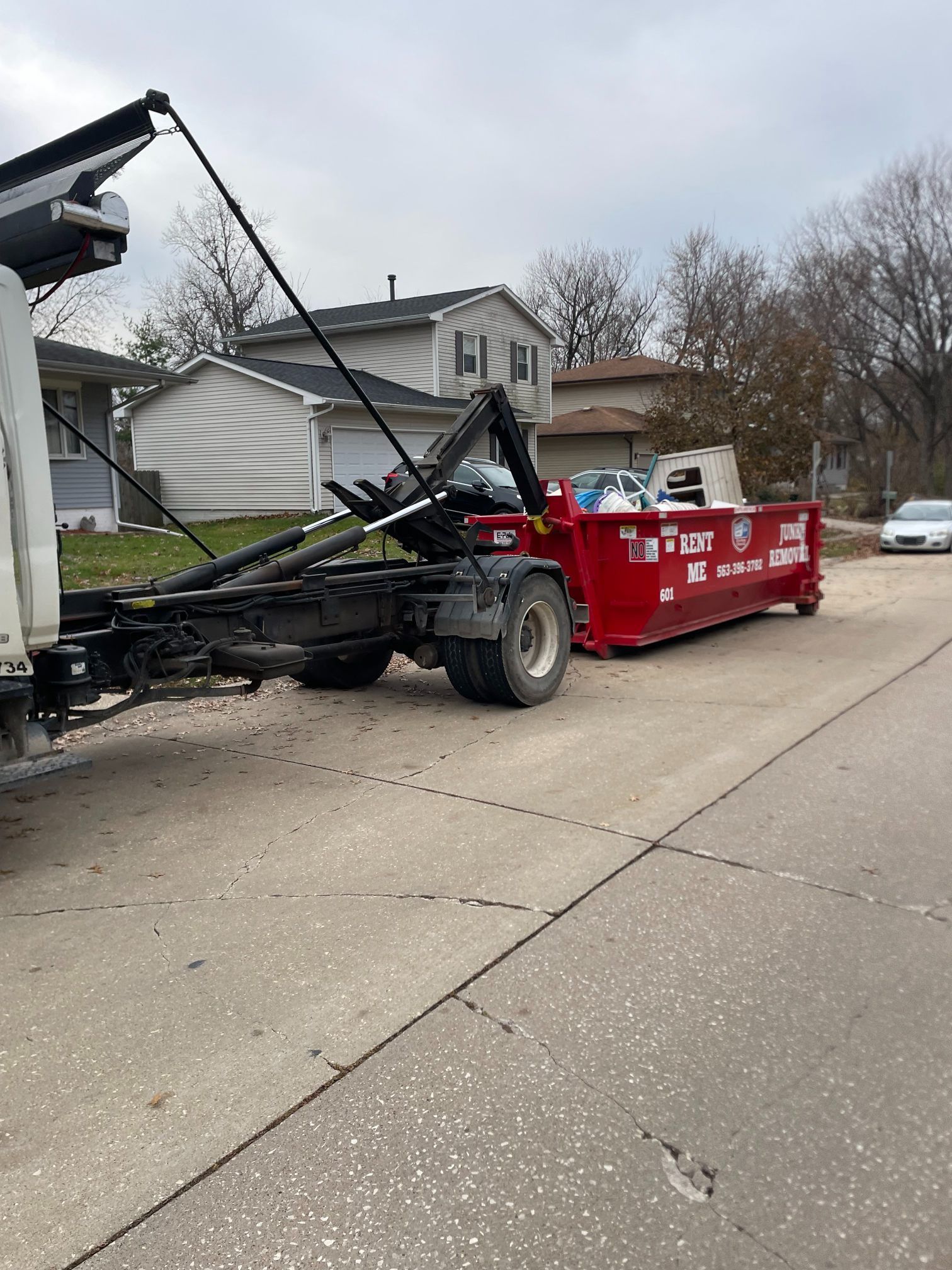 A red dumpster being loaded onto a truck on a residential street.