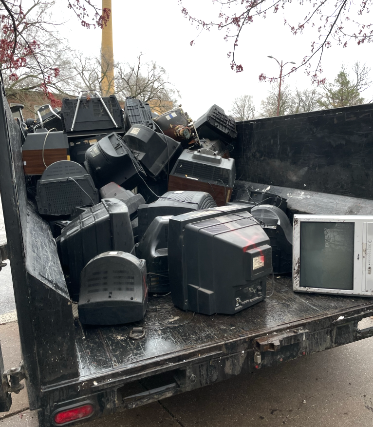 Dump truck bed overflowing with discarded CRT televisions.