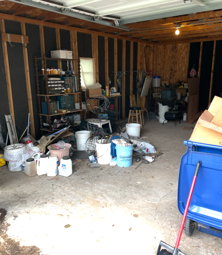 Cluttered garage interior with tools, containers, and shelves; blue bin in the foreground.