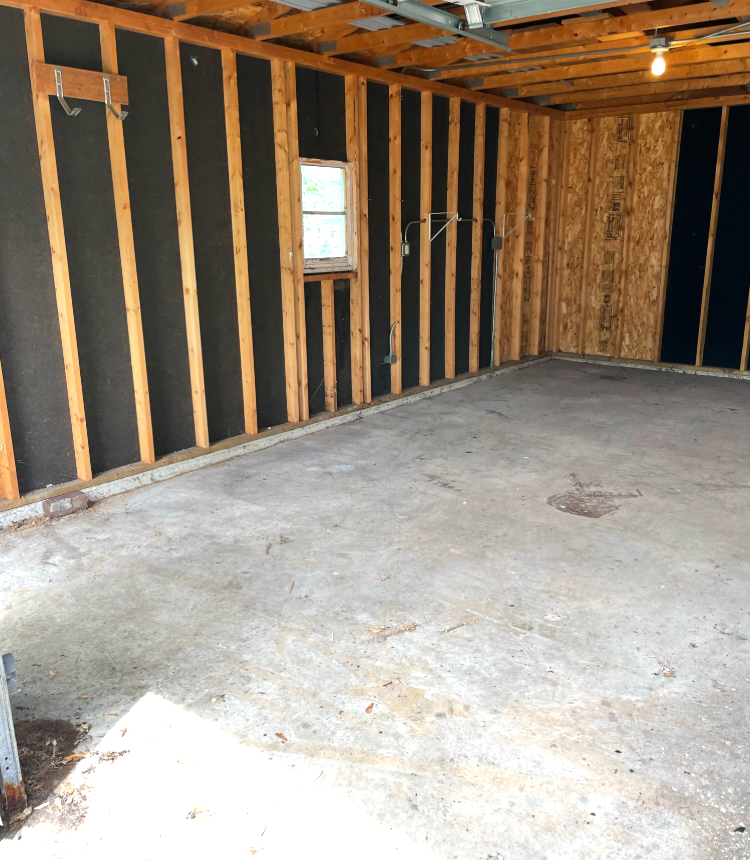 Interior of a garage with exposed studs and black insulation. Concrete floor, small window visible.