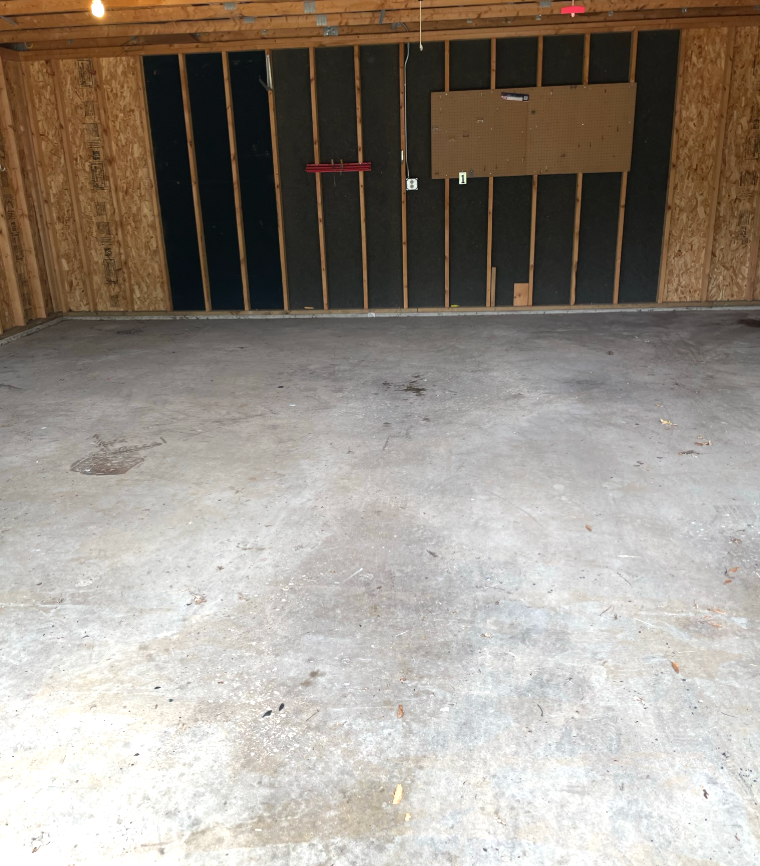 Empty concrete garage with wooden walls, part covered with black insulation.