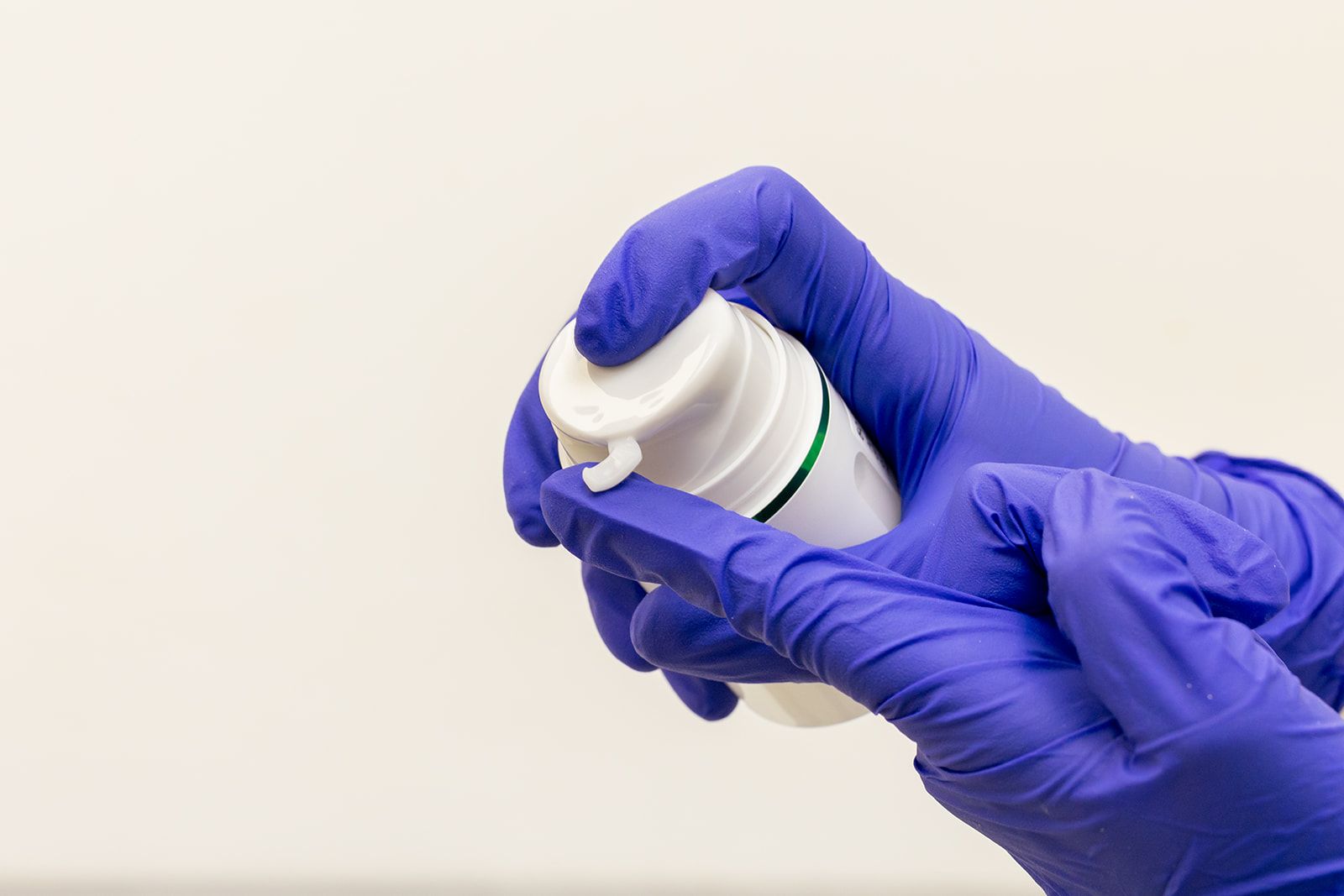 A person wearing purple gloves is holding a white bottle. A person wearing purple gloves is holding a white bottle.