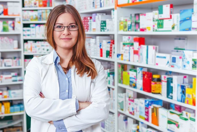 Cheerful female pharmacist standing by rows of medicine. Cheerful female pharmacist standing by rows of medicine.