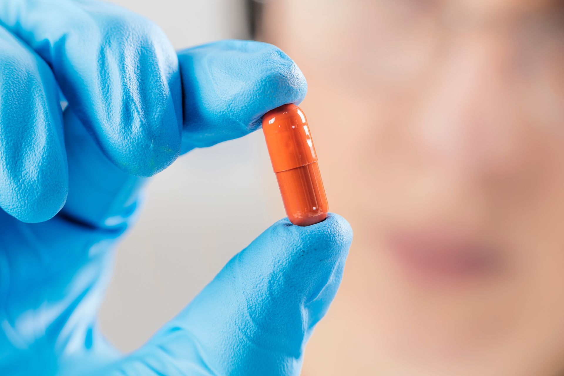 Close-up of a scientist’s hand in a blue glove holding an orange pill.