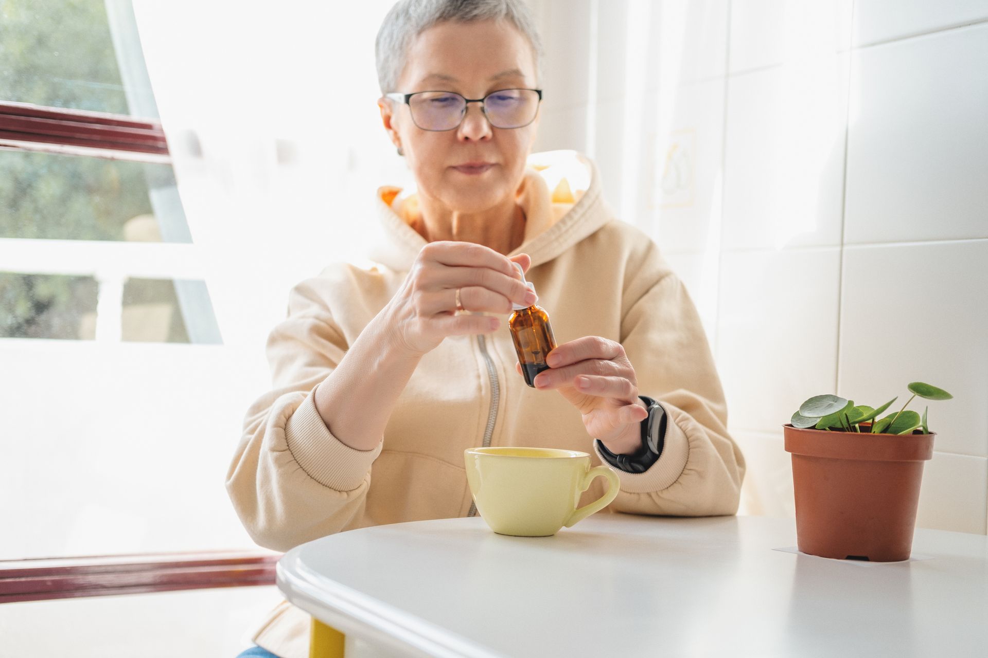 An elderly woman is sitting at a table eating a sandwich and drinking tea.