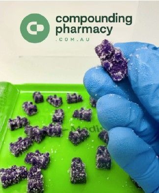 A gloved hand holding purple gummy bears. Green tray with more bears, compounding pharmacy logo.