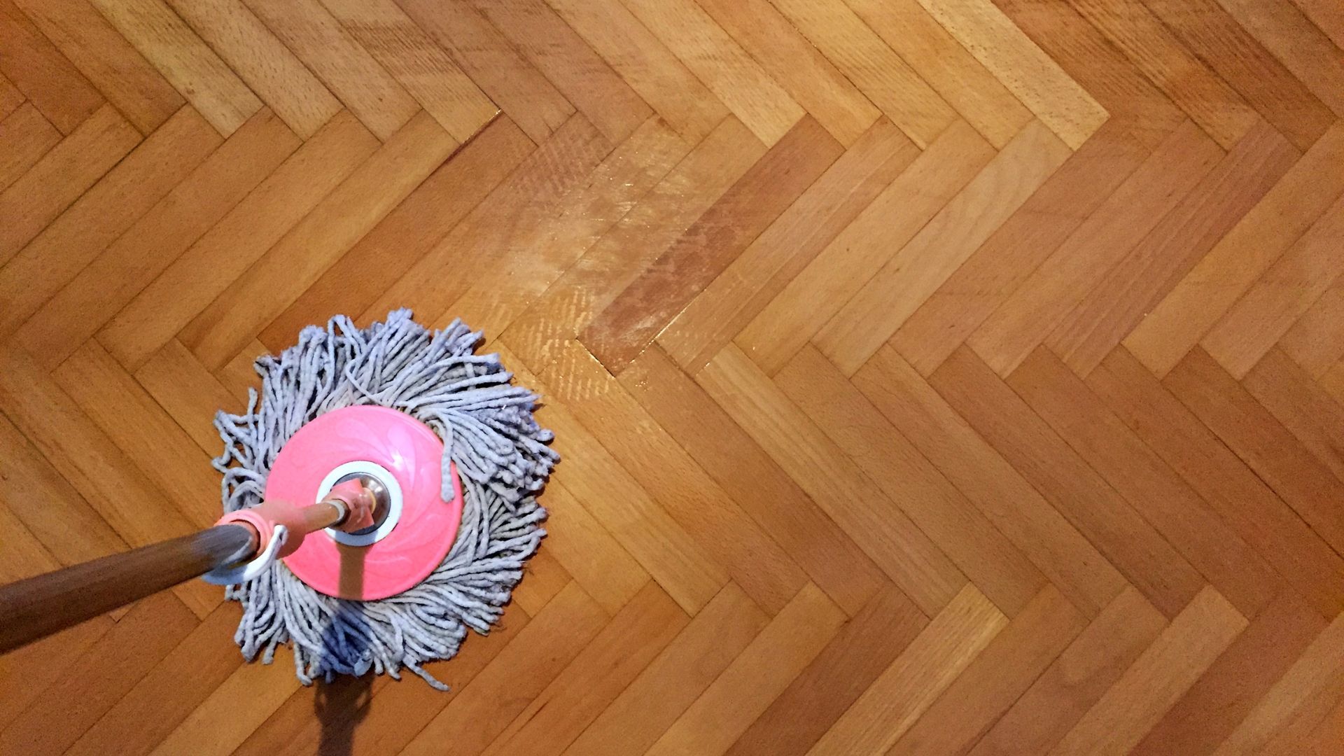 How to Clean Prefinished Hardwood Floors Shown with a pink mop cleaning a wood floor