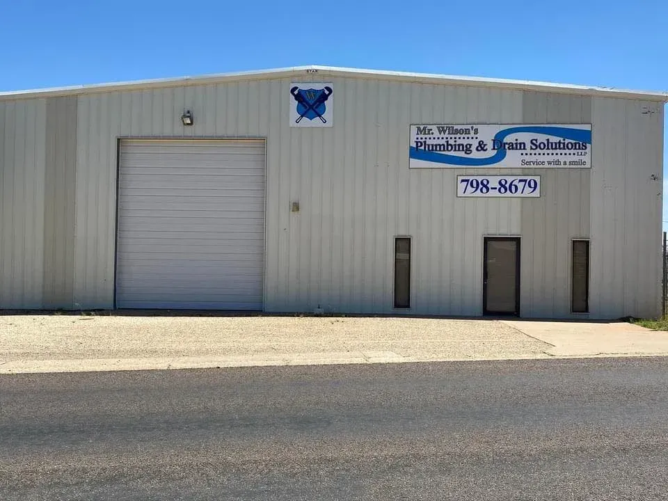 A white building with a blue sign that says plumbing and drain solutions