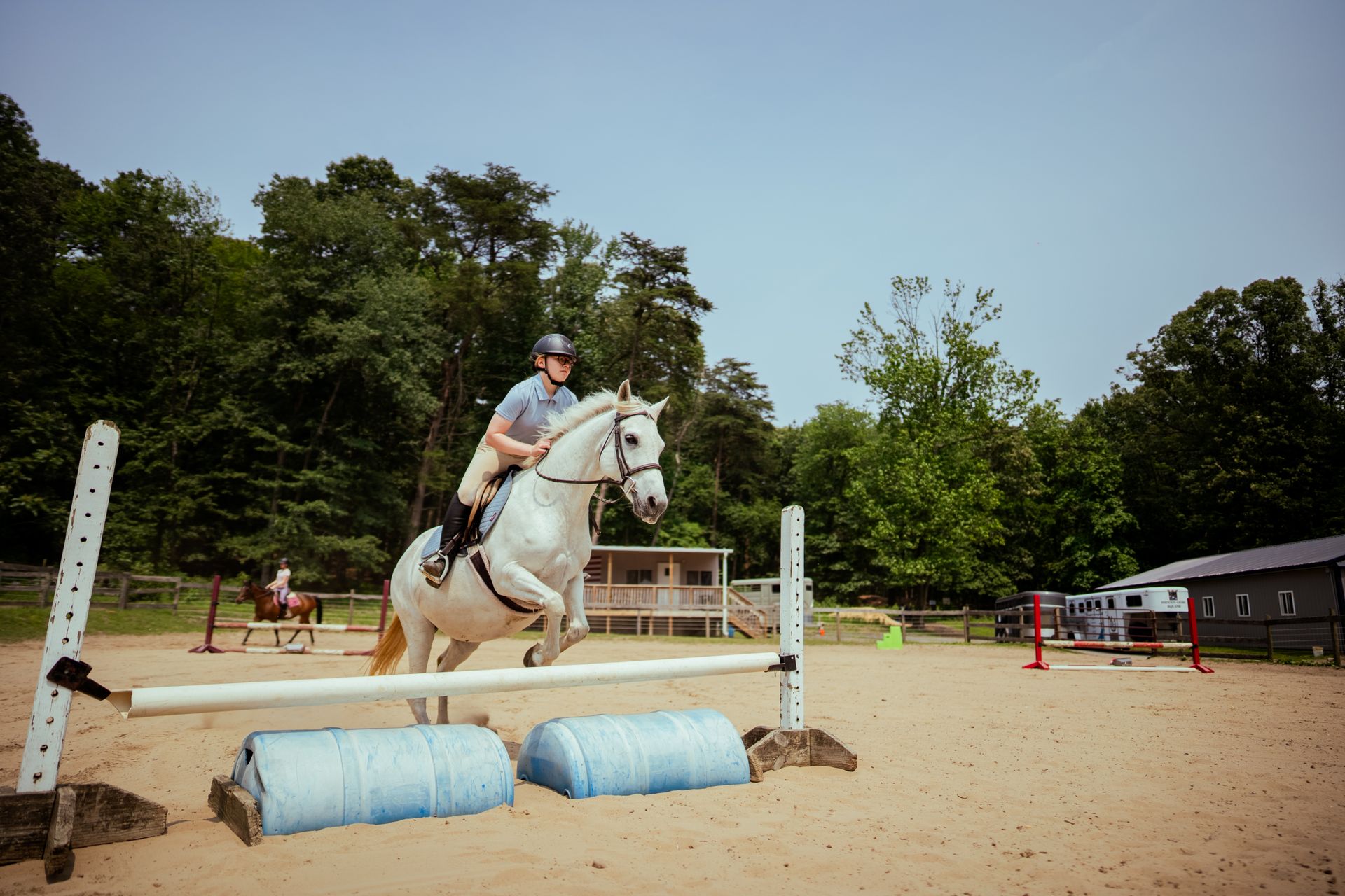 A person is riding a white horse over a jump.