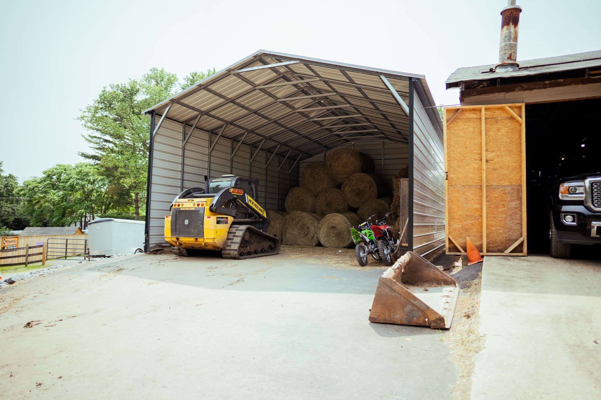 A truck is parked in front of a barn filled with hay bales.