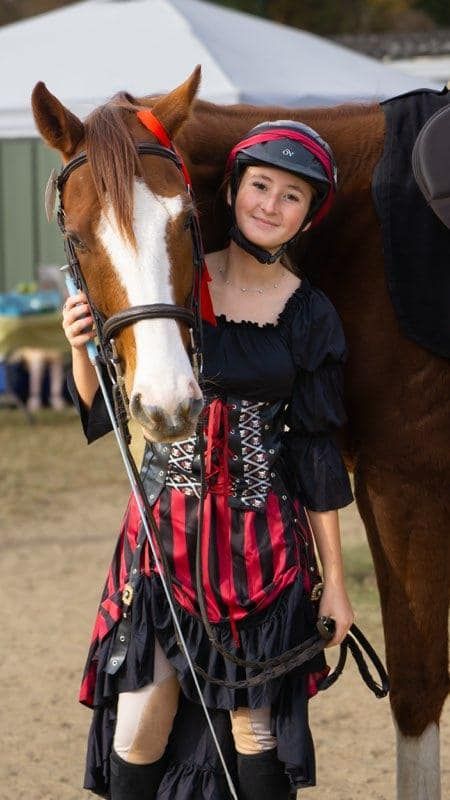A woman in a pirate costume is holding a brown horse