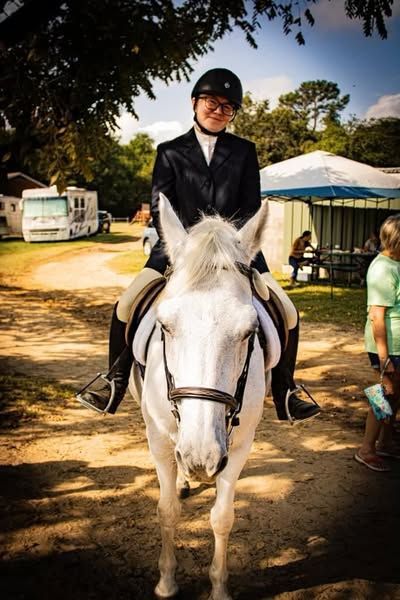 A woman is riding a white horse on a dirt road