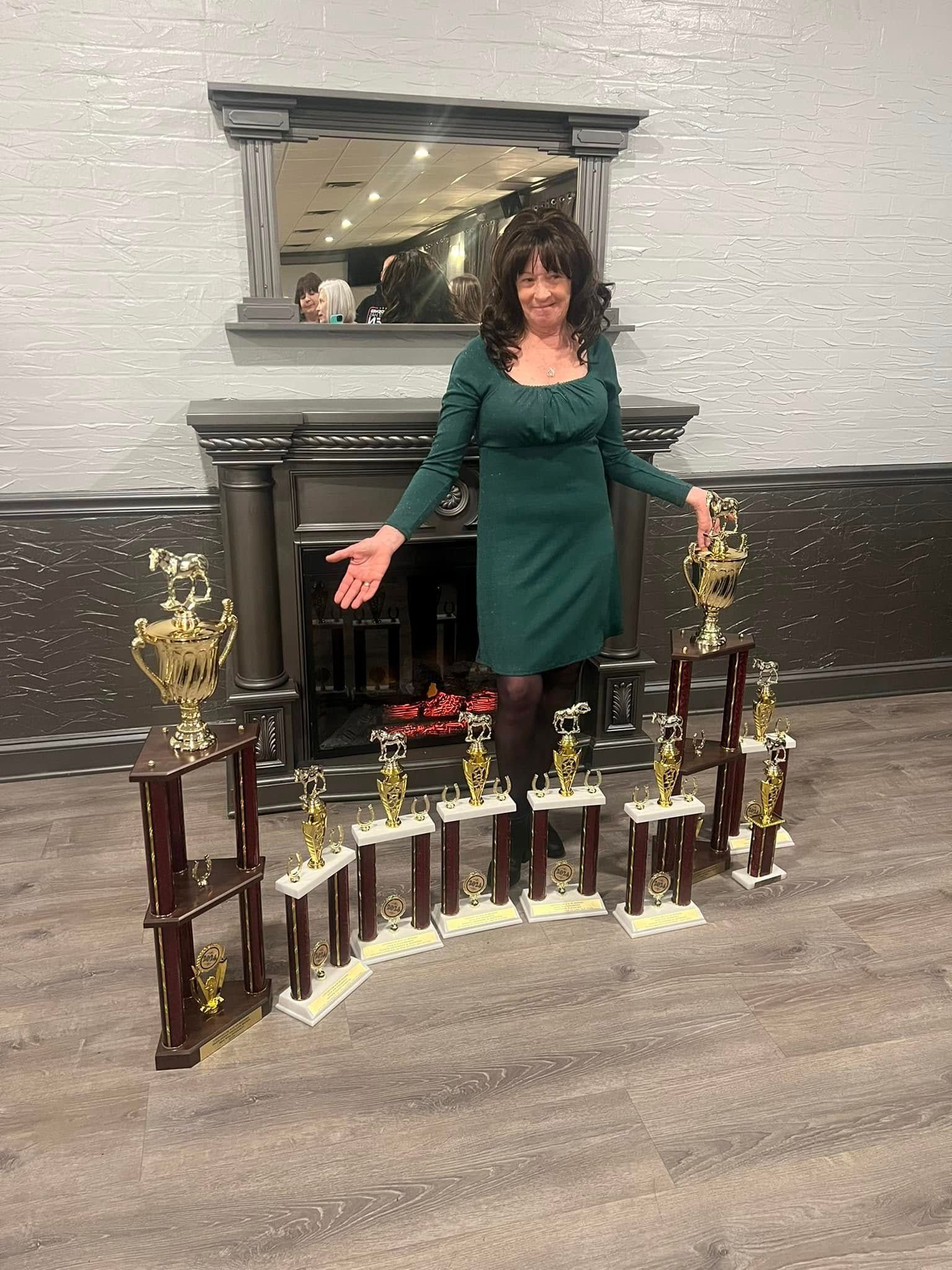 A woman in a green dress is standing in front of a fireplace holding trophies.