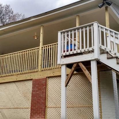 A wooden deck with lattice skirting and a white staircase leading to a covered patio.