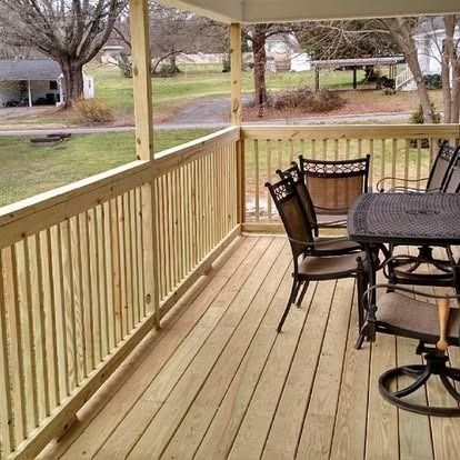 A view from a wooden deck with a railing looking out onto a grassy yard with bare trees and a house in the distance.