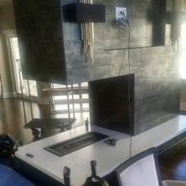 A modern indoor fireplace with a stone facade, white hearth, and hanging gold light fixture in a bright, open room.