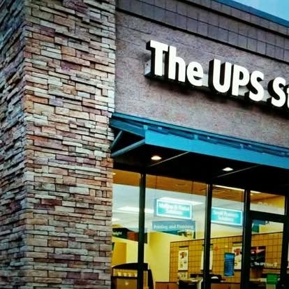 The storefront of The UPS Store, featuring a stone brick exterior, a dark blue awning, and glass windows.