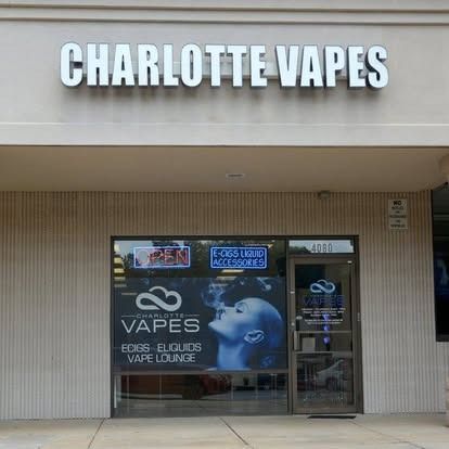 Storefront of Charlotte Vapes, a retail shop featuring branded signs and a window display showing a vaping person.
