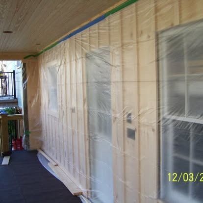 A porch wall covered in plastic sheeting for protection while wood siding is being installed, with a date stamp.