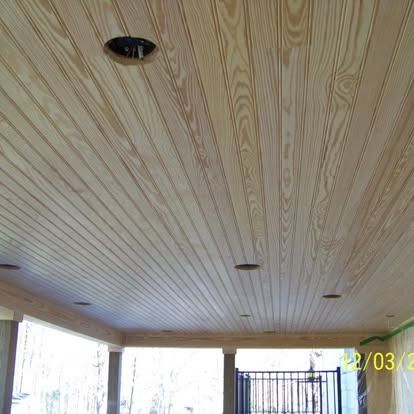A light-wood paneled ceiling with several circular recessed light cutouts on a covered outdoor patio.