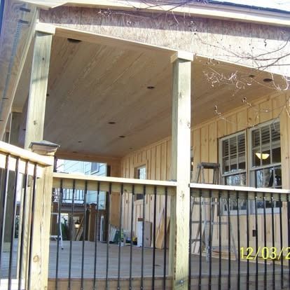 A wooden deck with black metal railings and recessed lighting under a covered porch attached to a light-sided house.