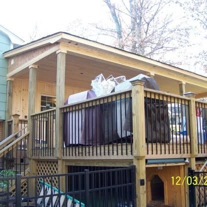 A wooden deck with a covered porch, a black metal railing, and a dog house underneath, set against a house.