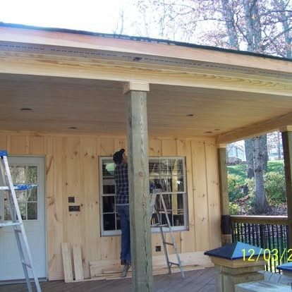 A worker on a step ladder installs wood siding on the exterior wall of a porch with a support post and deck.