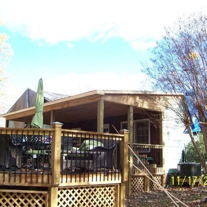 A wooden deck with black railings and lattice skirting attached to the side of a house, featuring an overhead patio roof.