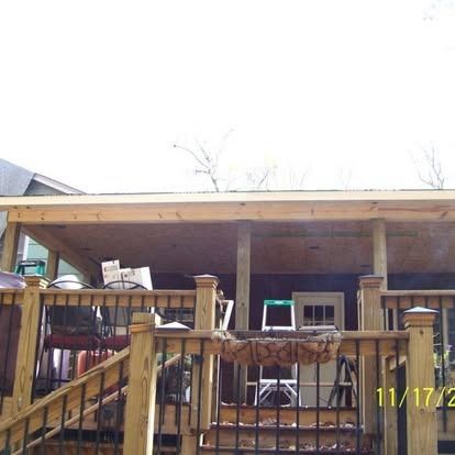 A wooden deck featuring a covered porch with a metal railing and a ladder visible under the roof.