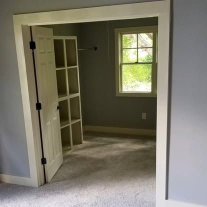 A view through an open doorway into a small closet with grey walls, a white shelving unit, and a window with a green view.