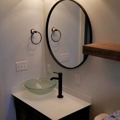 A modern bathroom vanity with a white countertop, a frosted glass vessel sink, a matte black faucet, and a round mirror.
