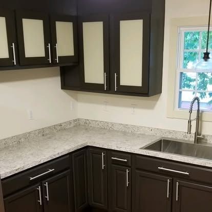 A modern kitchen corner featuring dark wood cabinets with glass insets, speckled granite countertops, and a steel sink.