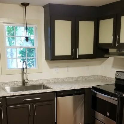 A modern kitchen with dark brown cabinets, frosted glass inserts, speckled countertops, and stainless steel appliances.
