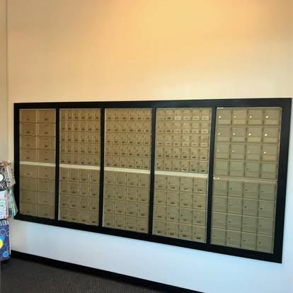 A large, wall-mounted unit of rectangular, brass-colored mailboxes arranged in five vertical columns within a black frame.