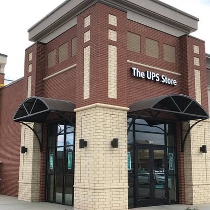 The corner entrance of a brick UPS Store building with two black arched awnings over glass doors.