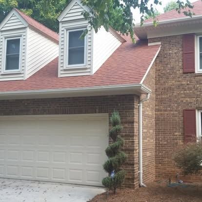 A two-story house with a brick exterior, red shingled roof, attached garage, and two dormer windows.