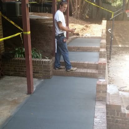 A person standing on new concrete steps with brick borders, holding a phone at an outdoor residential construction site.
