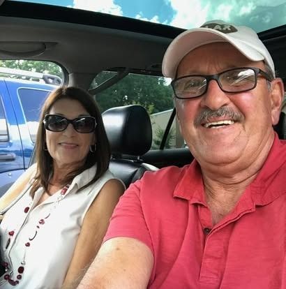 A man and woman sitting in the front seats of a car, both smiling at the camera.