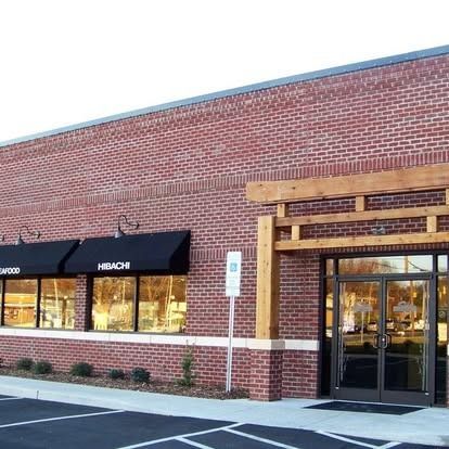 A brick commercial building with black window awnings and a wooden entryway frame under a clear sky.