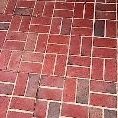 A close-up of a brick walkway featuring a herringbone pattern in varying shades of red and brown.