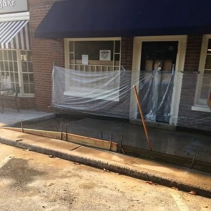 A freshly poured concrete sidewalk in front of a brick storefront, with plastic sheeting covering the window and door.